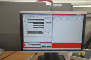 Monitor z oprogramowaniem MTS, wyświetlający wykresy i dane pomiarowe. Kluczowe obiekty: monitor, oprogramowanie, wykresy.