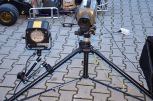 Kamera wideo na statywie i lampa oświetleniowa. W tle widoczny gokart.