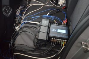 Elektronika z licznymi przewodami na siedzeniu samochodu. Kluczowe obiekty: urządzenia elektroniczne, kable, siedzenie.