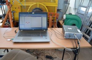 Laptop z oprogramowaniem, urządzenie pomiarowe i wentylator. Kontekst: stanowisko badawcze.