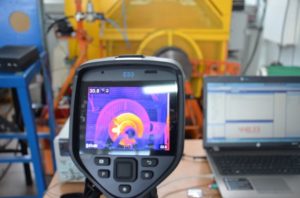 Kamera termowizyjna FLIR E53 analizuje temperaturę elementu maszyny. Obok laptop z danymi.