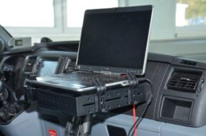 Laptop zamontowany na desce rozdzielczej pojazdu. Kluczowe obiekty: laptop, uchwyt, deska rozdzielcza.