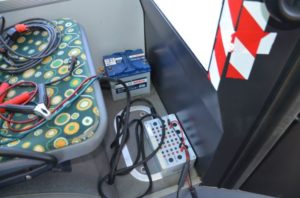Akumulator Bosch, kable rozruchowe i tester podłączone do siedzenia w pojeździe.