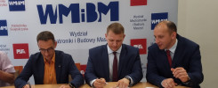 Trzech mężczyzn w garniturach podpisuje dokumenty przy stole. W tle logo Politechniki Świętokrzyskiej.