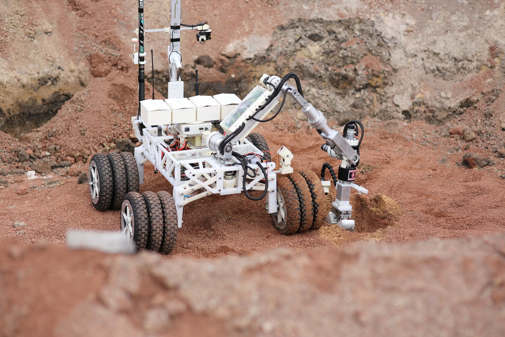 Robot z ramieniem i kamerą na kołach, badający teren. Kontekst: eksploracja.