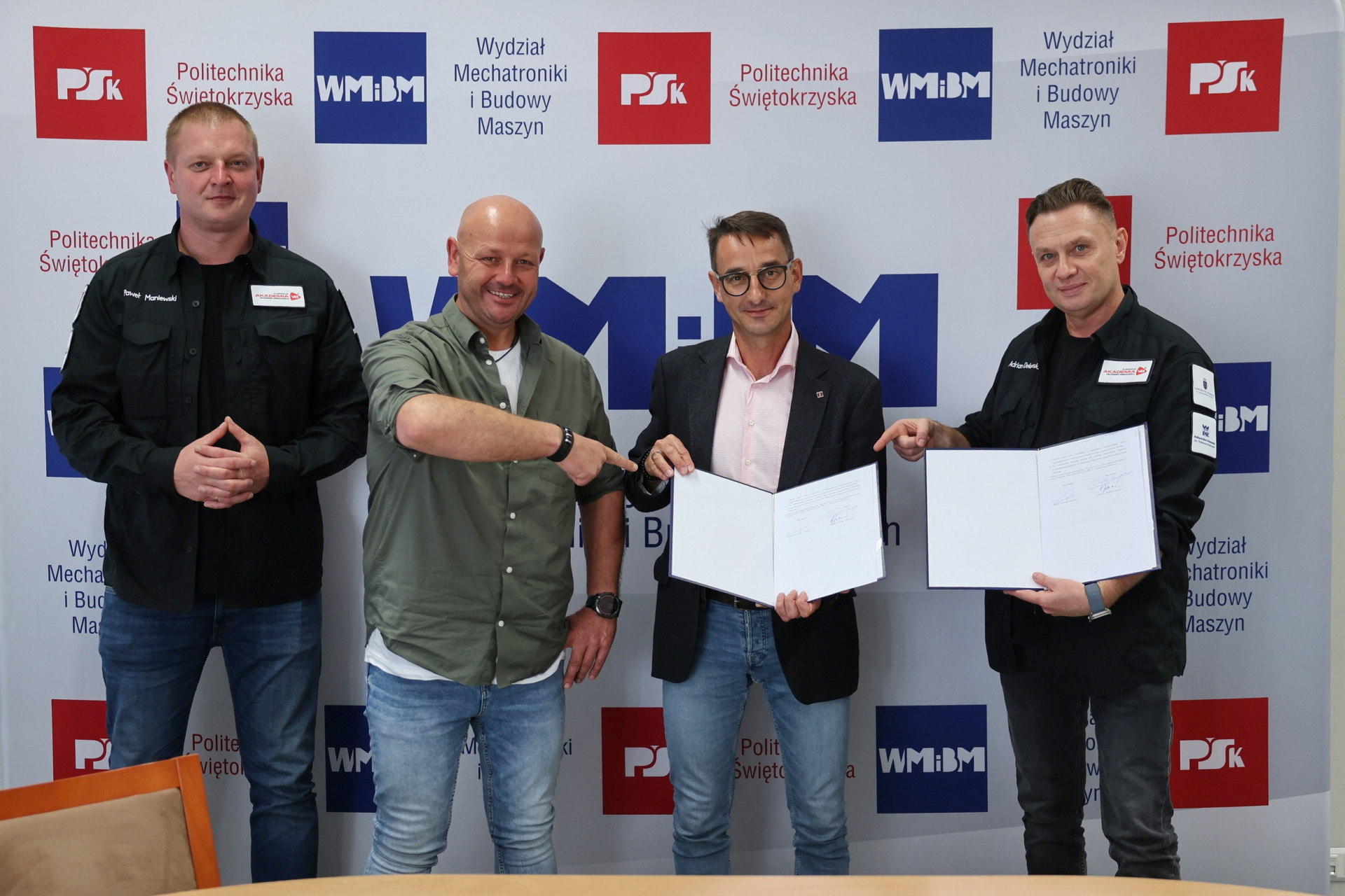 Czterech mężczyzn stoi przed banerem Politechniki Świętokrzyskiej. Dwóch trzyma otwarte dokumenty.
