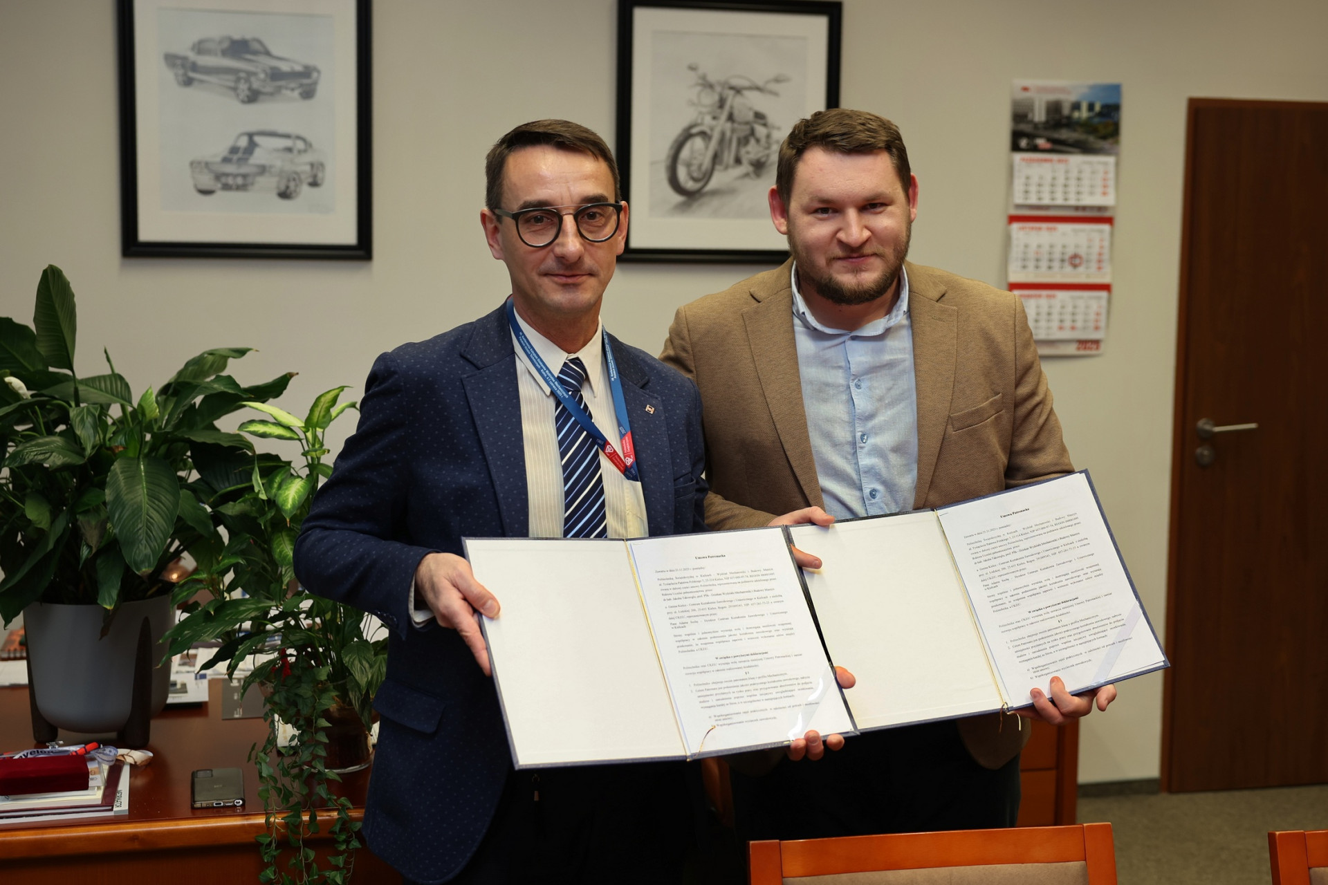 Dwóch mężczyzn trzyma otwarty dokument. W tle obrazy samochodów, motocykla i kalendarze.