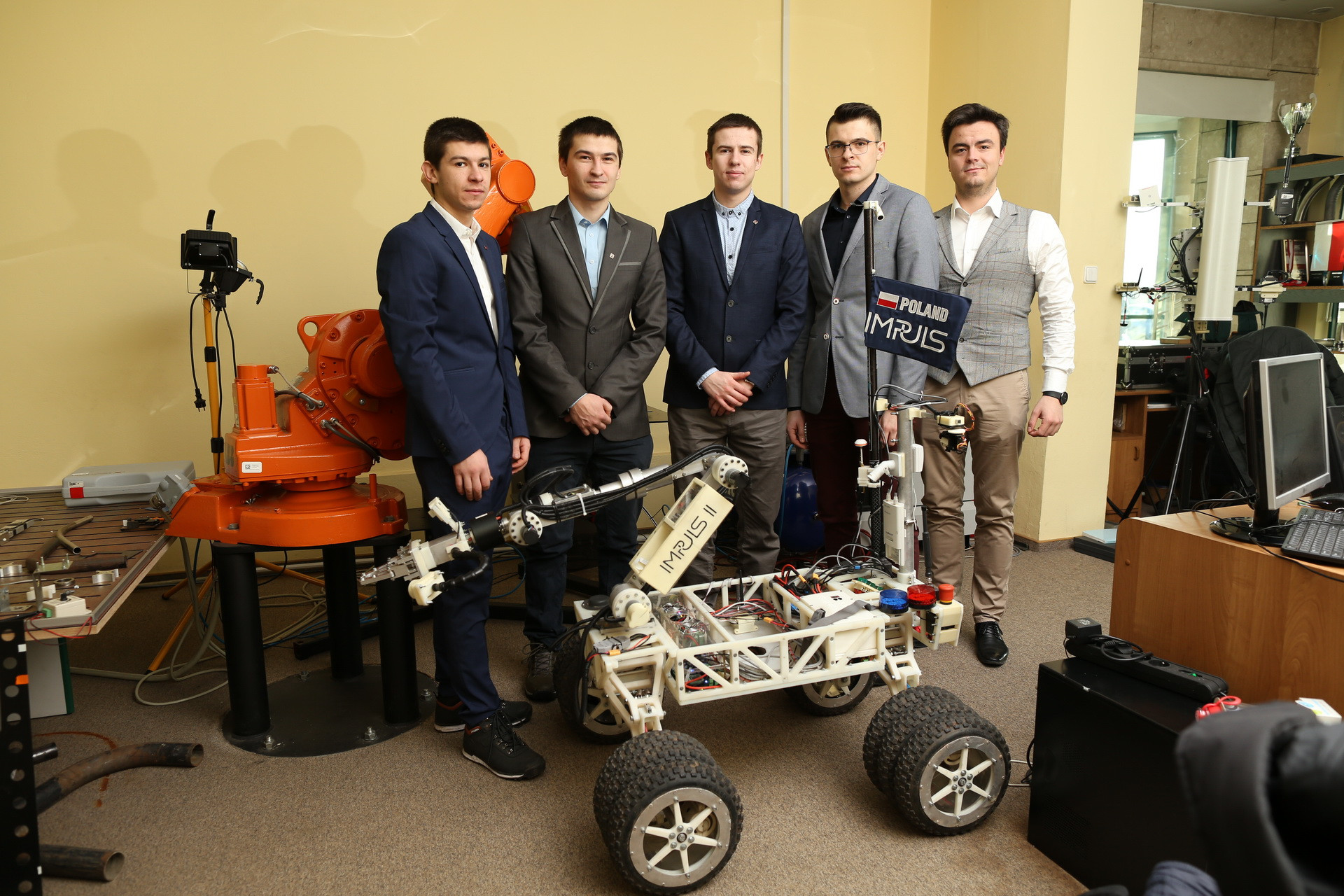 Pięciu mężczyzn pozuje obok robota mobilnego i ramienia robota.