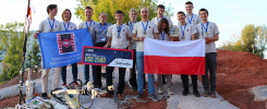 Grupa młodych ludzi z Politechniki Świętokrzyskiej z flagą Polski i nagrodą. Kluczowe obiekty: robot, flagi, nagroda, ludzie.