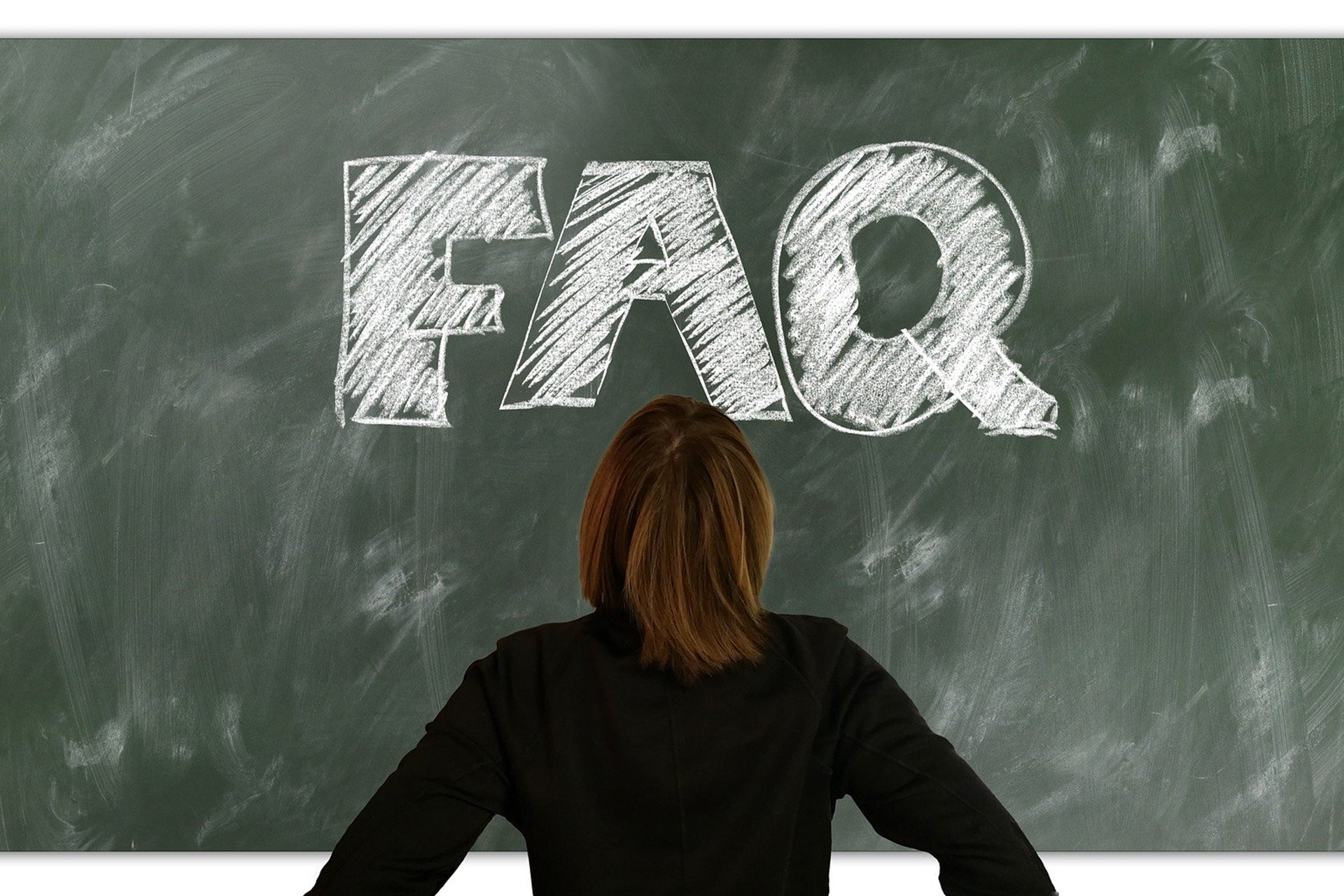 Osoba patrzy na tablicę z napisem "FAQ" napisanym kredą. Kontekst: edukacja, pytania i odpowiedzi.
