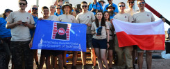 Grupa osób trzyma polską flagę i baner Politechniki Świętokrzyskiej. Kluczowe obiekty: ludzie, baner, flaga, budowla.