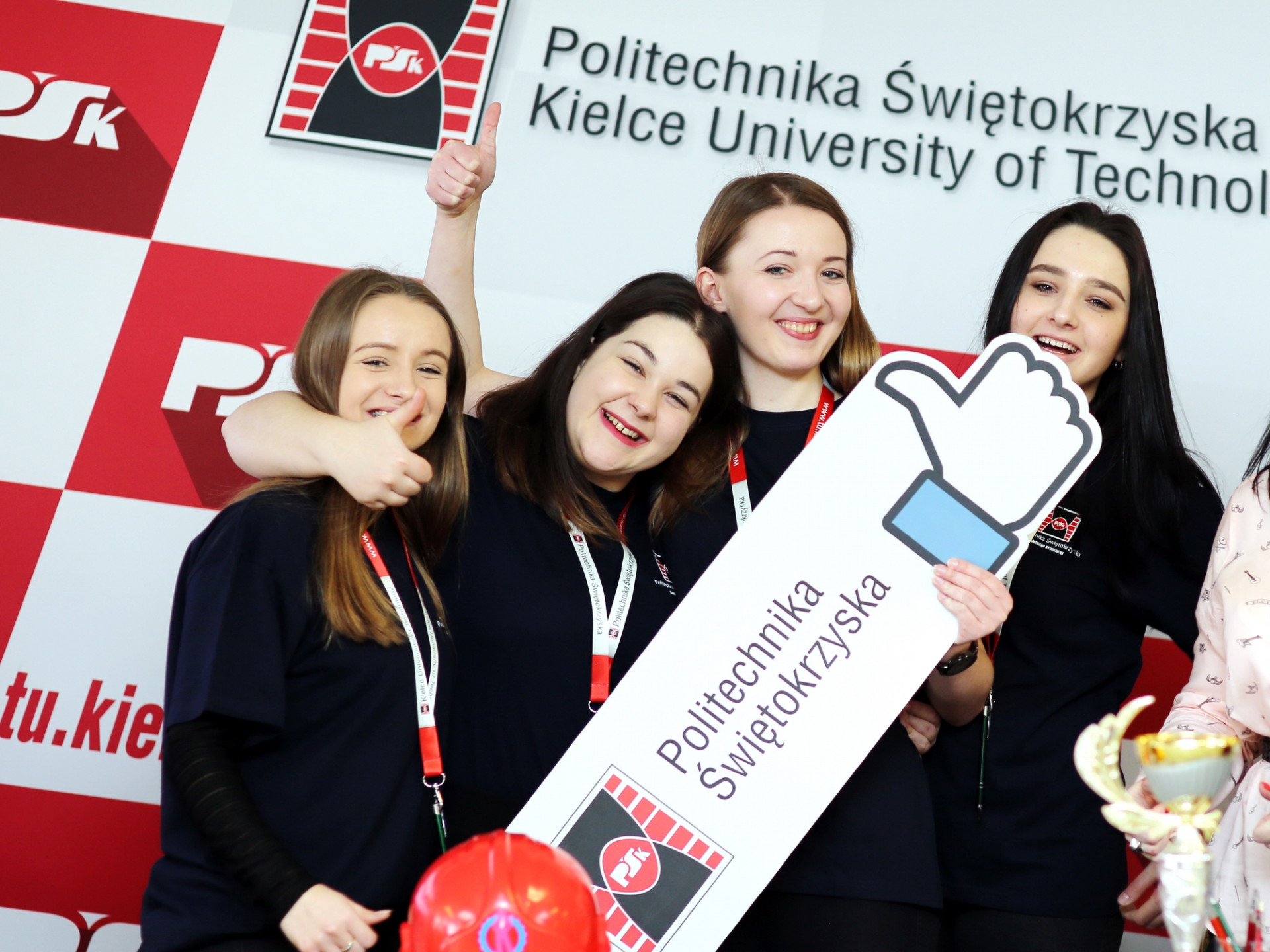 Cztery młode kobiety pozują z tabliczką "Politechnika Świętokrzyska". W tle logo uczelni.