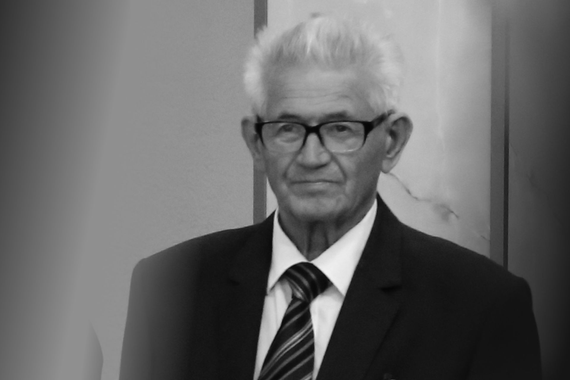 Czarno-białe zdjęcie starszego mężczyzny w okularach, garniturze i krawacie.