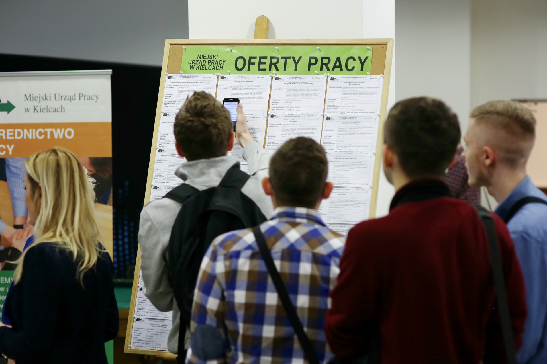 Tablica z ofertami pracy Miejskiego Urzędu Pracy w Kielcach. Ludzie oglądają ogłoszenia.